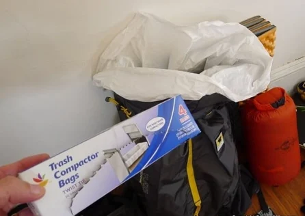 Box of heavy-duty trash compactor bags held up beside a backpack lined with one to keep gear dry