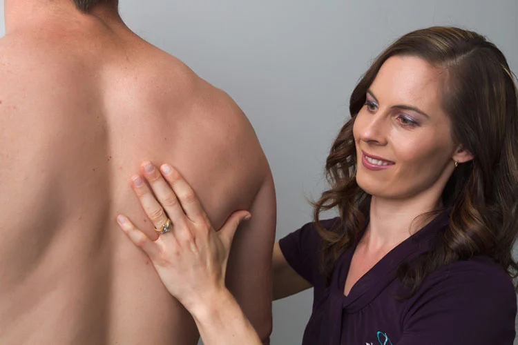 Therapist placing her hand on a man's shoulder blade to assess and treat the muscles of the upper back