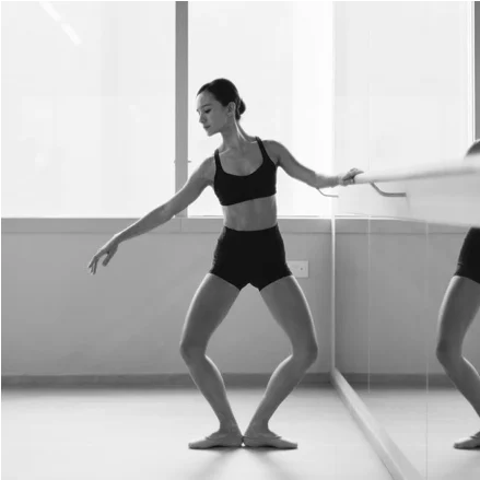 Dancer at a ballet barre in a turned-out plié, knees bent over the toes with one arm extended