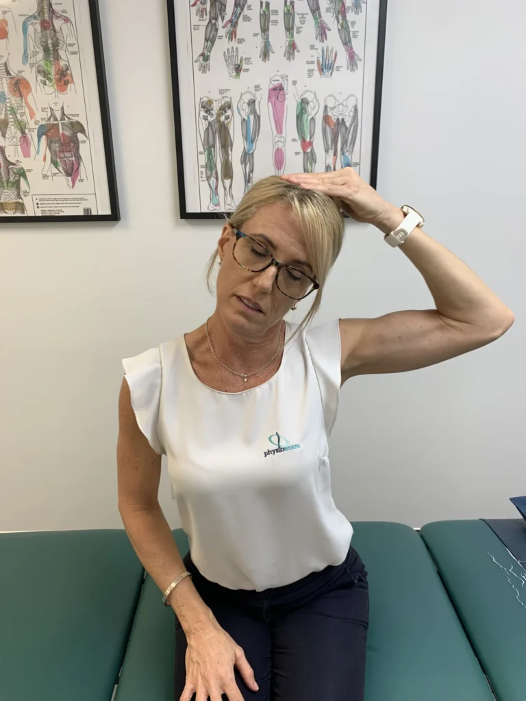 Woman seated, tilting her head to the side with one hand resting on top of her head to deepen a neck stretch