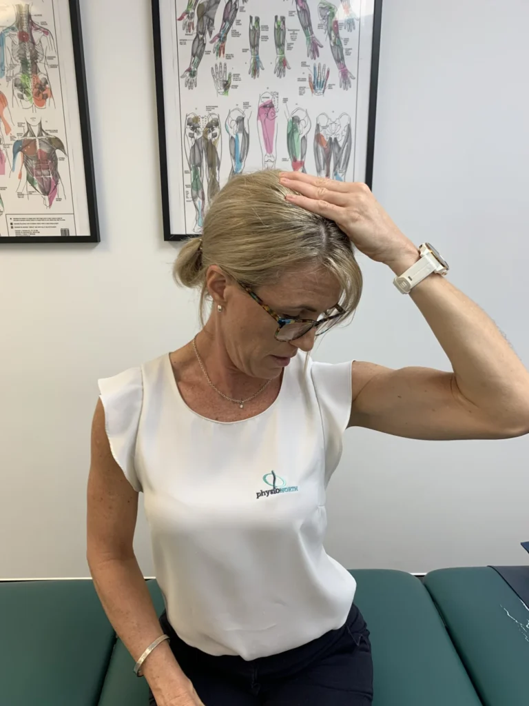 Woman seated, turning her head down towards one armpit and using her hand on the back of her head to stretch the neck