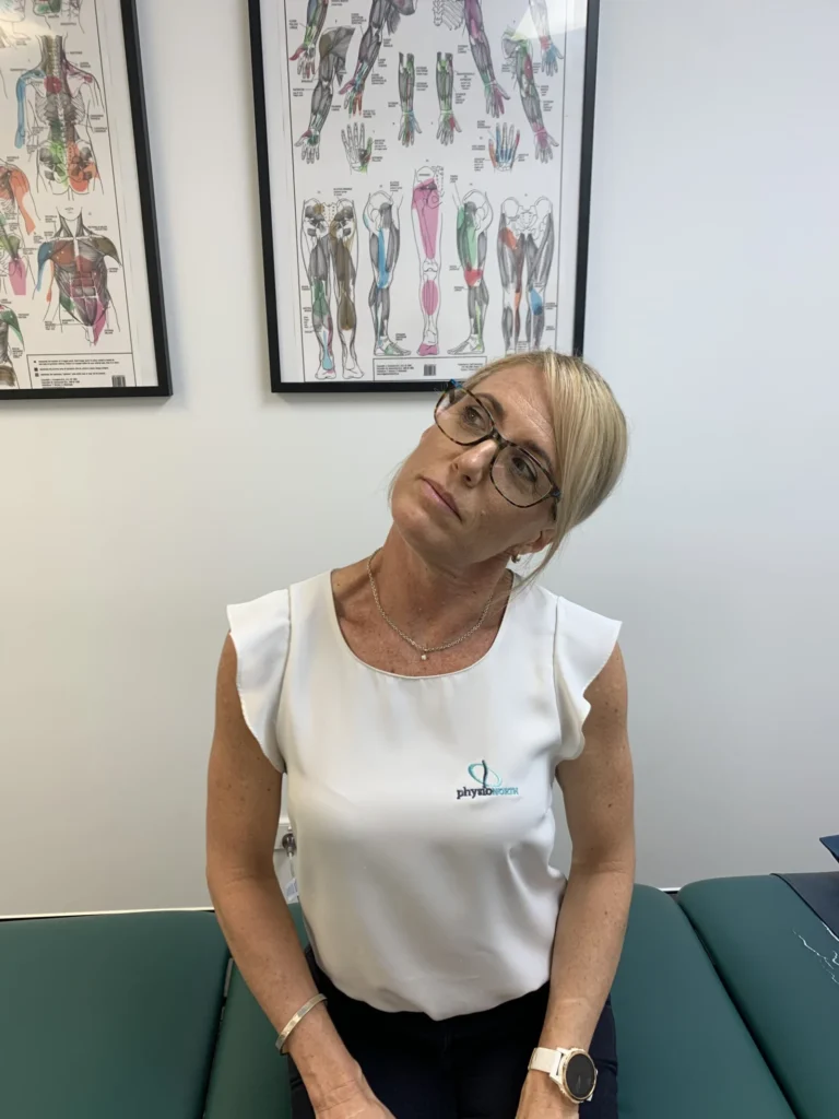 Woman seated, tilting her head to one side, ear towards shoulder, to stretch the side of the neck