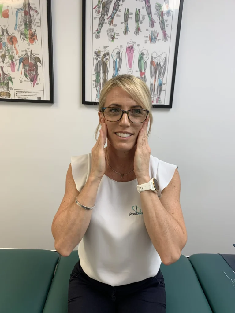 Physiotherapist seated with her fingertips on both cheeks, massaging the masseter jaw muscles