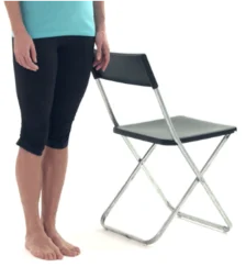 Person standing barefoot beside a chair, ready to hold the backrest for support during balance exercises