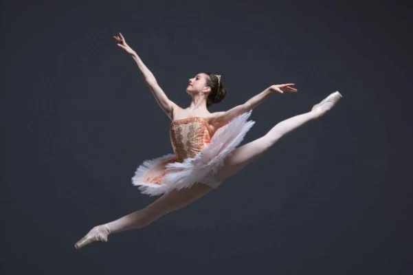 Ballet dancer in a tutu mid-leap in a full split, arms extended