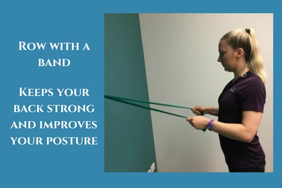 Woman standing facing a wall, pulling a resistance band back towards her body in a row to keep the back strong