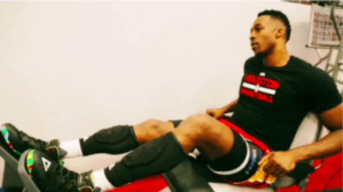 Basketball player seated on a leg press machine wearing knee sleeves during a blood flow restriction session