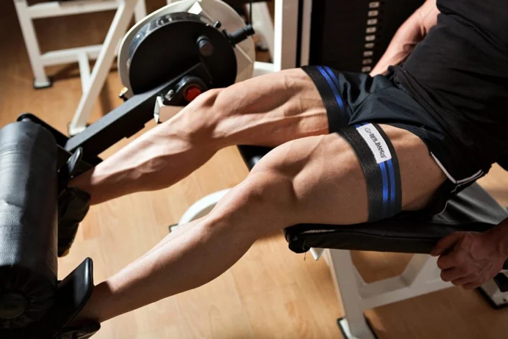 Person doing a seated leg extension machine with blood flow restriction bands wrapped around the upper thighs