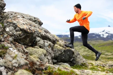 Trail runner leaping up a rocky outcrop on a mountain trail, one knee driving high