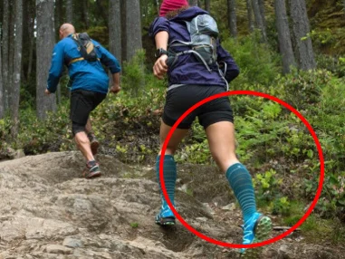 Two trail runners climbing a rocky uphill path, with the calf muscles of the front runner circled