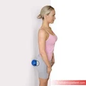Woman standing with her back to a wall, a massage ball pressed between the wall and her buttock to release the glutes