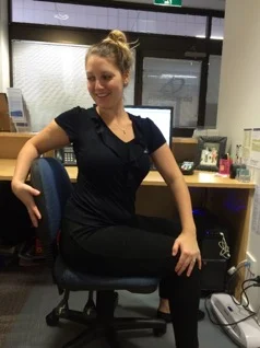 Woman seated on an office chair with legs crossed, twisting her trunk to one side and holding the chair back to stretch