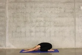 Person in child's pose on a yoga mat, kneeling with hips back on heels and arms stretched forward along the floor