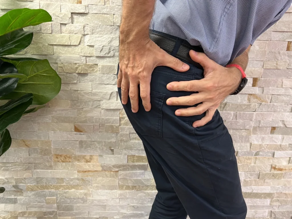 Person holding the outside of their hip with both hands, showing where hip bursitis pain is felt