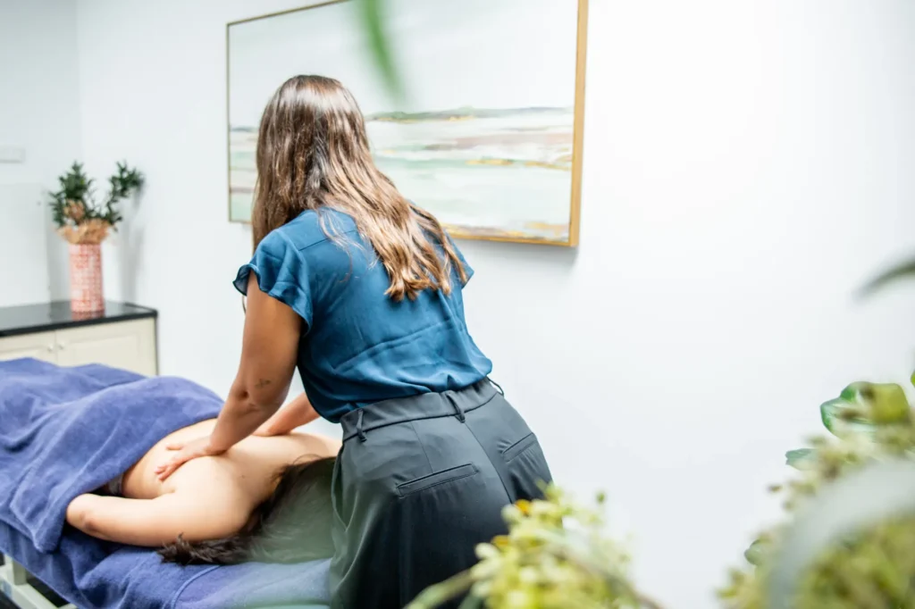 A remedial massage therapist leaning in to work deeply through a patient’s back