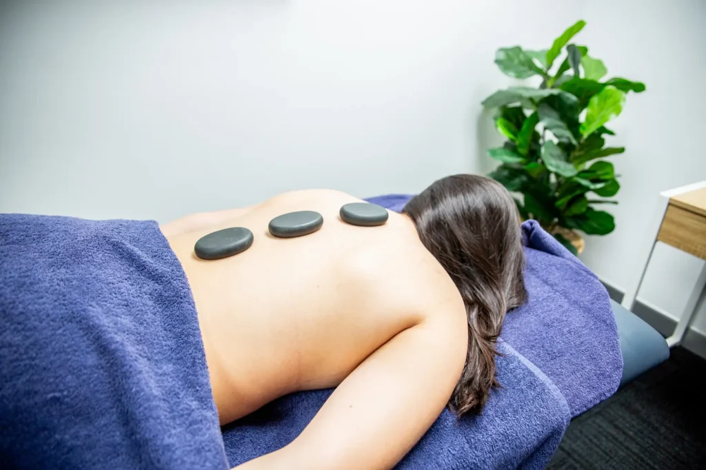 Smooth warm stones resting along a patient’s spine in a massage room