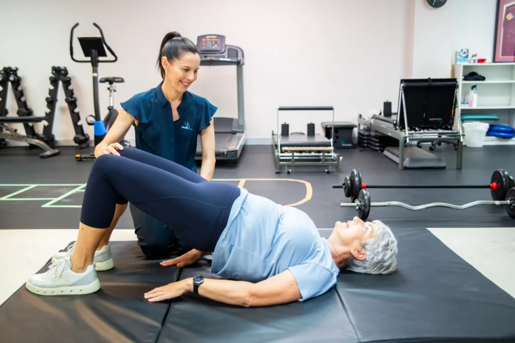 A physiotherapist guiding a patient through a bridging exercise on a mat