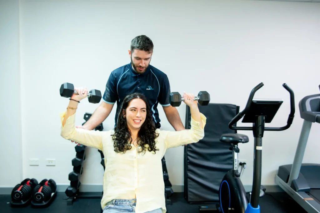A physiotherapist supervising an overhead dumbbell exercise